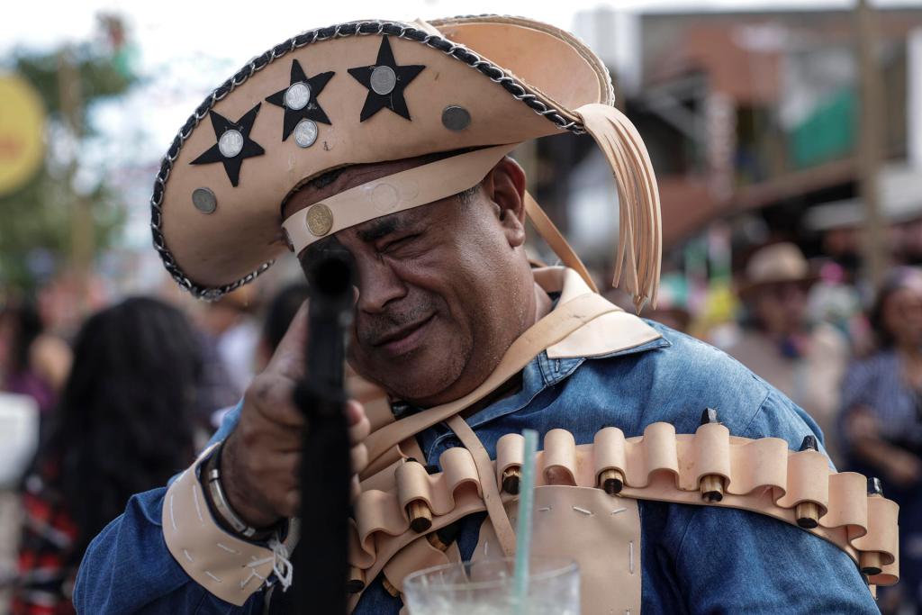 Un hombre con ropa típica de la historia de Pernambuco, apunta una arma falsa durante los festejos de la Fiesta de San Juan, el 10 de junio de 2023 en la región de la ciudad de Caruaru, interior del estado de Pernambuco, noreste de Brasil.. EFE/Antonio Lacerda