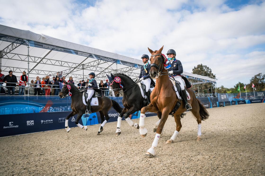 Fotografía cedida por FEI que muestra a Sarah Tubman, Codi Harrison, Anna Marek y Christian Simonson mientras celebran su victoria durante la ceremonia de entrega de medallas de doma clásica por equipos en los Juegos Panamericanos 2023. EFE/ Cortesía FEI