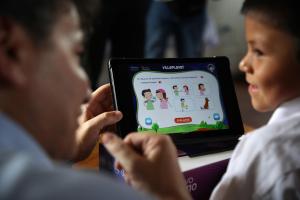 Fotografía de una persona junto a un niño manipulando una tableta en la institución educativa Miguel Grau, en la localidad de Miguel Grau, departamento de Ucayali (Perú). EFE/ Paolo Aguilar