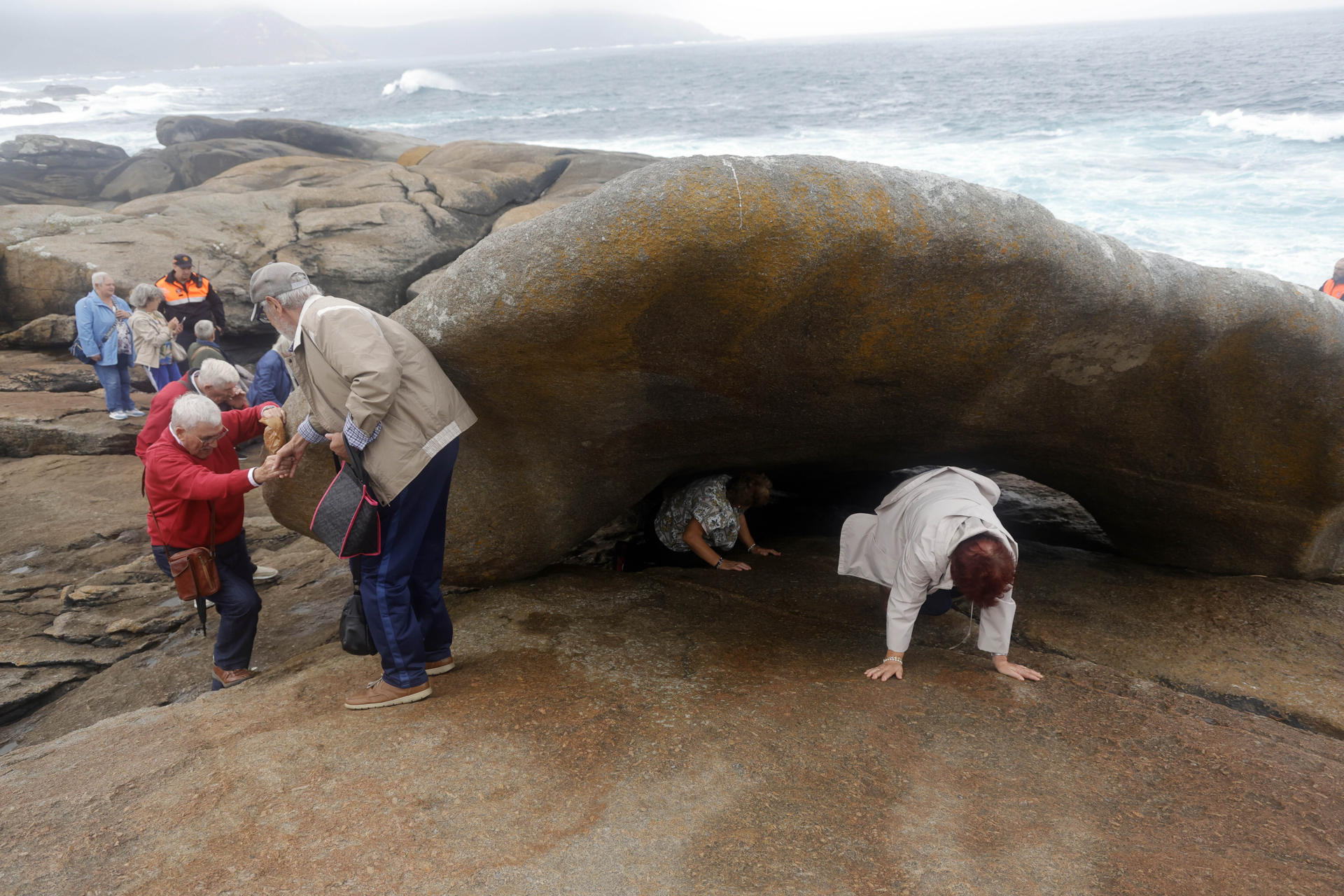 MUXIA (CORUÑA), 14/09/2025.- Fieles pasa bajo la Pedra dos Cadrís tal y como manda la tradición durante la romería de la Virxe da Barca, que este 2025 ha captado el interés de medios internacionales, este domingo en Muxia. EFE/Kiko Delgado